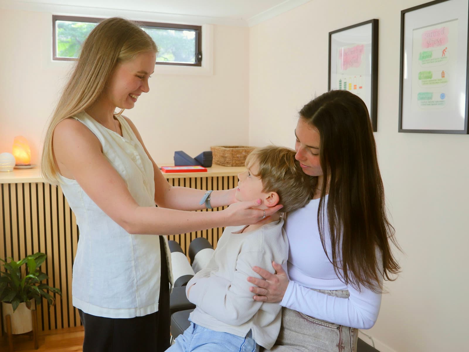 Dr Lucy gently checking a young boy's neck while he sits on his mum's lap